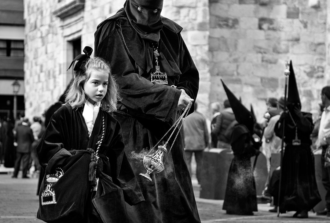 Una niña junto a un participante con túnica oscura y un incensario.